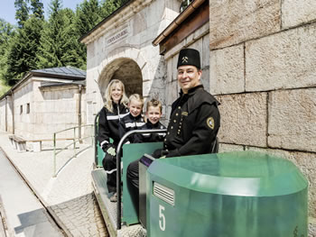 Die urige Grubenbahn im Salzbergwerk Berchtesgaden bringt die zahlreichen Besucher in das Innere des Bergwerks.Die rustikale Fahrt ist für Jung und Alt ein echtes Erlebnis. Sie vermittelt das Gefühl wie die Bergleute noch heute in die Tiefe des Berges  täglich vorstoßen. Das geschulte  Grubenpersonal sorgt hierbei für eine sichere Fahrt in das Innere des Berges.(Familie mit Kind bei strahlendem Sonnenschein vor der Einfahrt in das  Salzbergwerk)